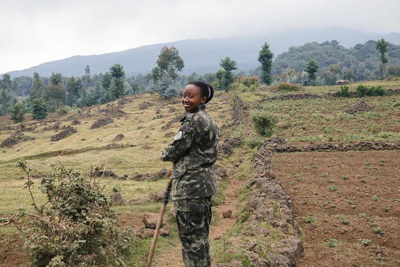 A conservation ranger standing near farmland and forested hills in Rwanda
