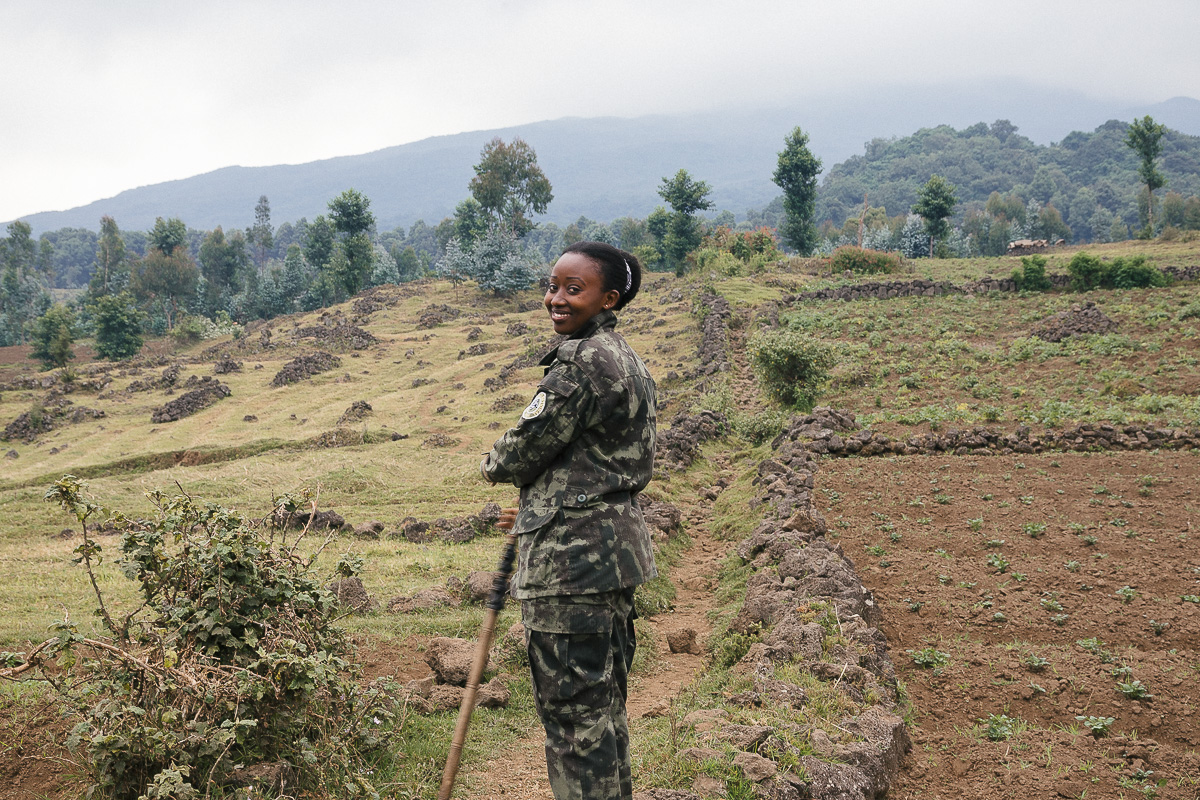 A conservation ranger standing near farmland and forested hills in Rwanda